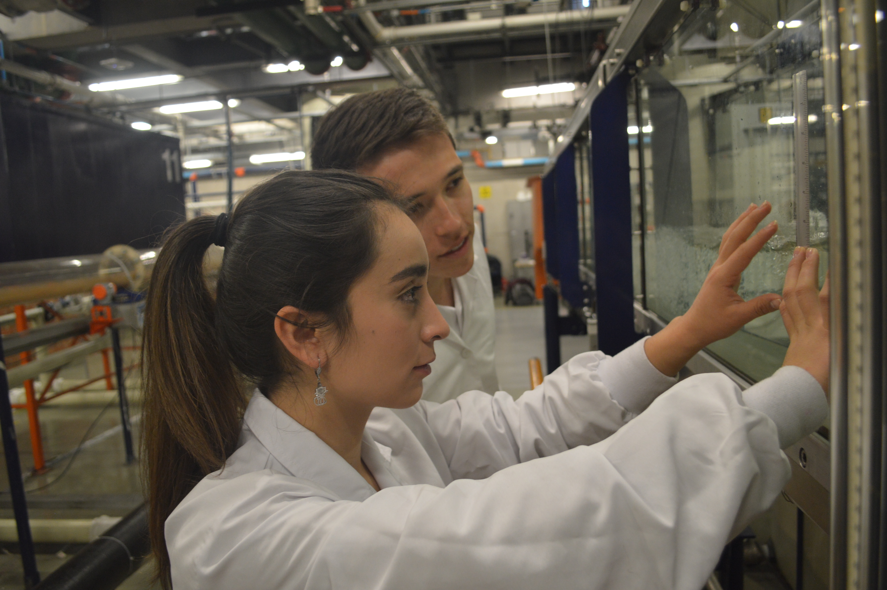 Dos estudiantes observando una muestra en una cámara de laboratorio. 